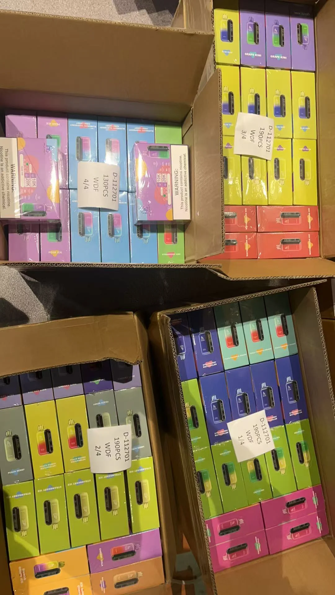 Multiple open cartons filled with colorful disposable vape packages sorted by flavor and labeled with quantity signs.