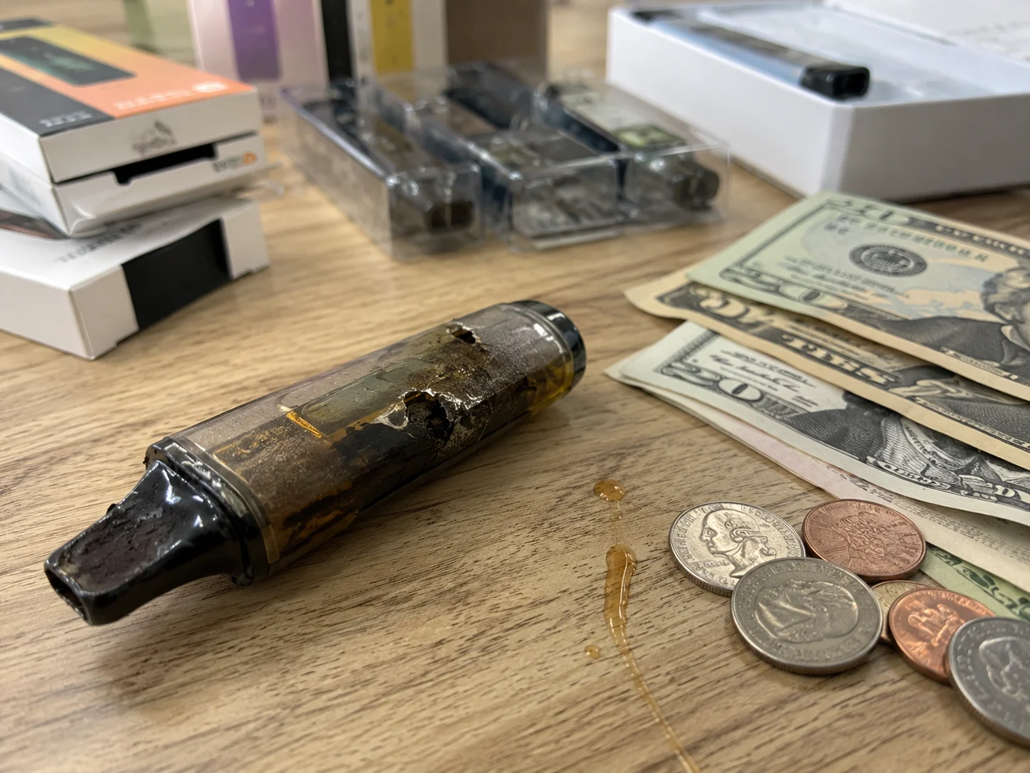 A broken disposable vape next to a pile of money