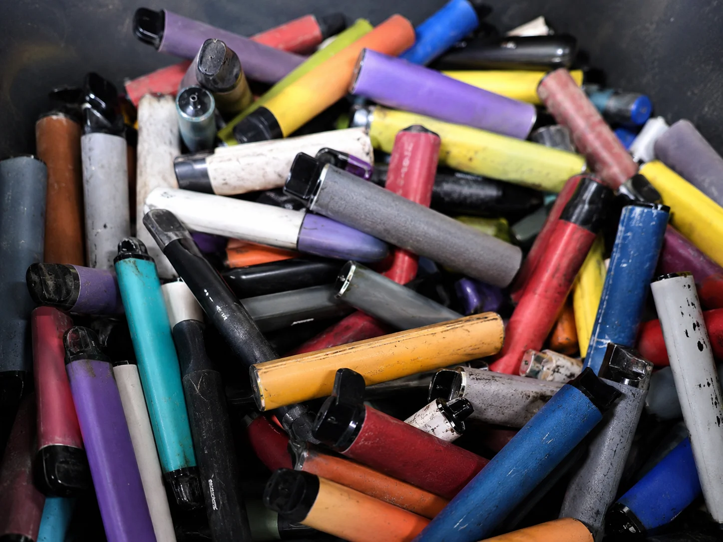A large pile of used disposable vape devices in various colors stored for recycling purposes.